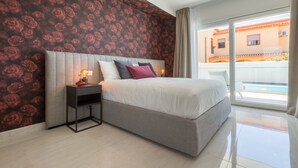 Un dormitorio con una cama grande, una mesita de noche con lámpara, papel tapiz floral y vistas a una piscina a través de un ventanal.