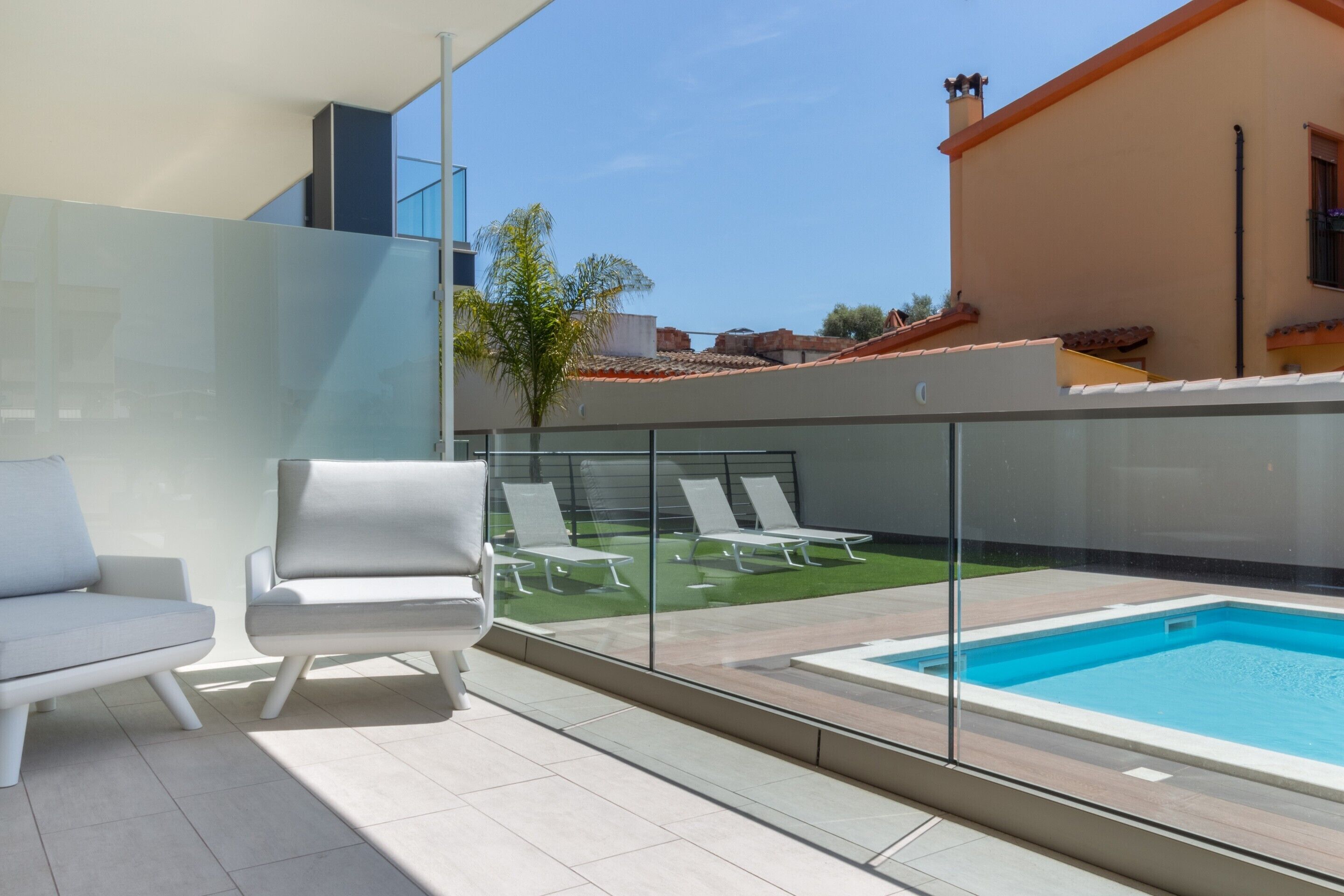 A modern outdoor pool area with lounge chairs and a glass barrier.