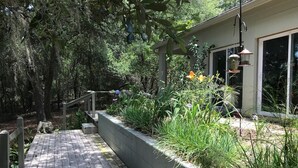 Eine Holzterrasse mit einem Pflanzkasten, der mit Pflanzen gefüllt ist, einer kleinen Treppe und einem Gebäude mit einem Fenster und einem Laternenvorbau.