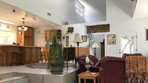 Ein großzügiger Wohnbereich mit Sofa, Couchtisch und Topfpflanze. Im Hintergrund ist eine Küchenzeile mit Schränken und einer Arbeitsplatte zu sehen.