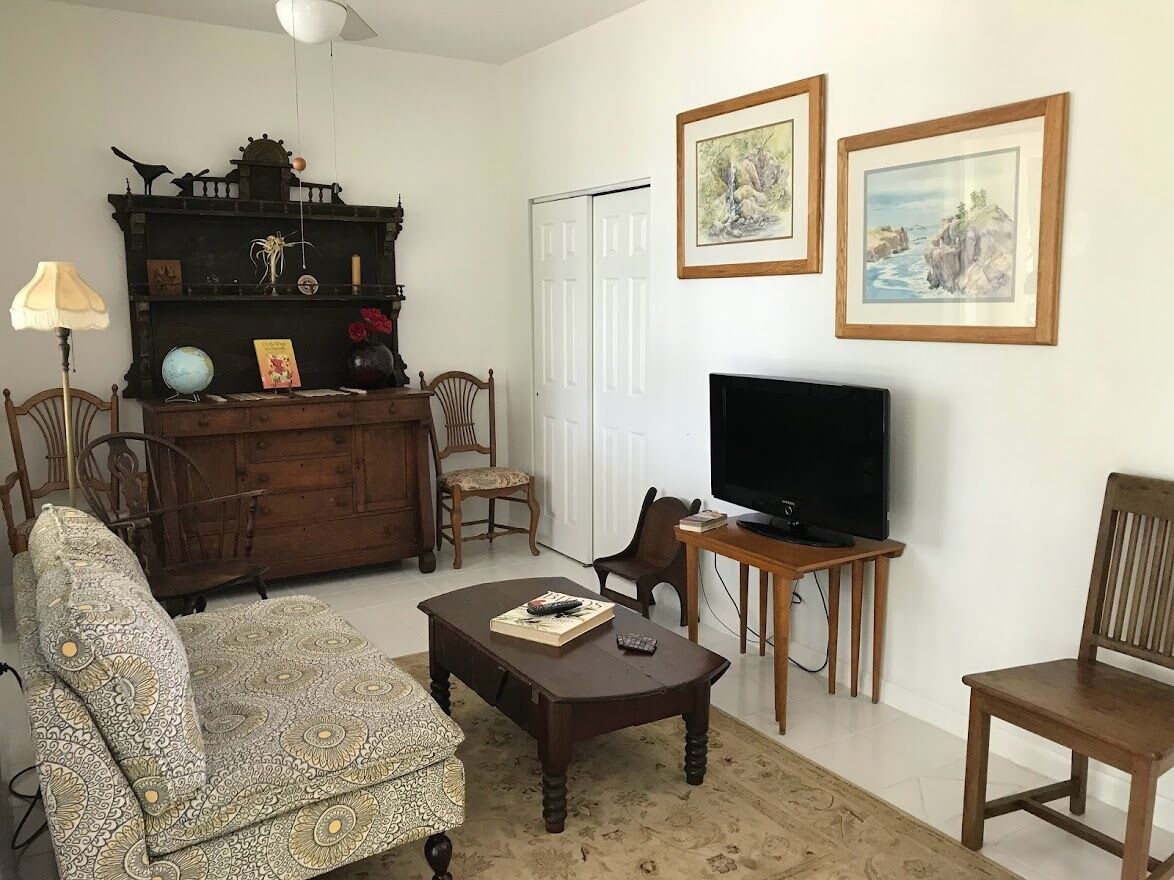 A living room with a sofa, armchair, wooden coffee table, TV, bookshelf, and framed pictures on the wall.