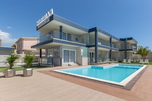 Una casa moderna de dos plantas con piscina, barandillas de cristal y techo plano.