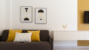Ein modernes Wohnzimmer mit einer Couch, Kissen, einem Flachbildfernseher und abstrakter Wandkunst.