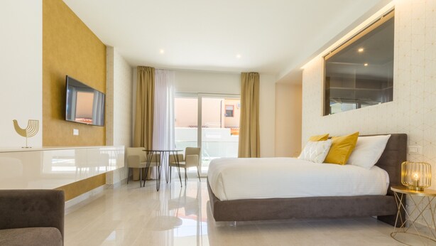 Ein modernes Hotelzimmer mit einem großen Bett, einem an der Wand befestigten Fernseher, einer Essecke mit Stühlen und Blick ins Freie.