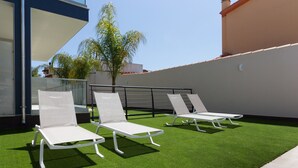 Eine Dachterrasse mit künstlichem Gras, weißen Liegestühlen und einem Glasgeländer.