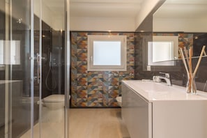Une salle de bain moderne avec une douche à parois de verre, des toilettes, un lavabo avec un miroir et un mur décoré d’un motif.