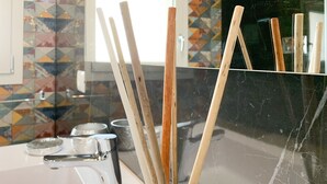 Un baño con un lavamanos moderno, un recipiente de vidrio con palitos de madera y un rebozado de azulejos.