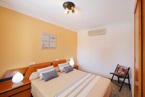 Une chambre d’hôtel avec un lit, des tables de chevet, un climatiseur fixé au mur et un tableau encadré accroché au mur.
