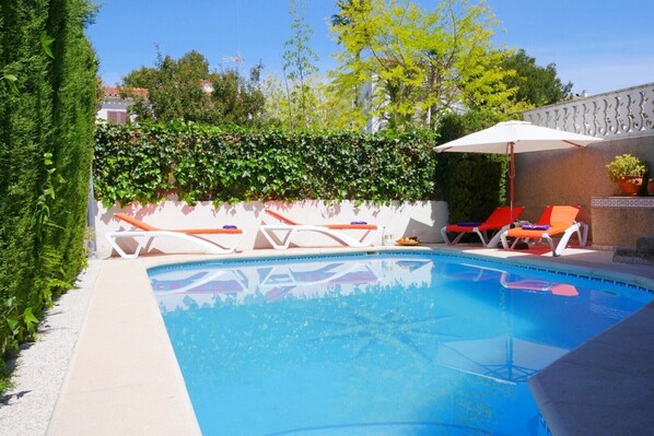 Une piscine avec des chaises longues et un parasol blanc.