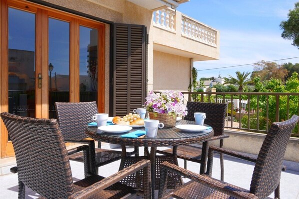 A round table with wicker chairs, a basket of flowers, and a plate of food on an outdoor balcony.