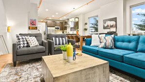 A modern living room with grey and blue sofas, a coffee table, and a kitchen in the background. - Wondrous Woodstock Townhouse, Huge Open Floor Plan, Custom Décor and Artwork, Four Miles to Portland (Portland)