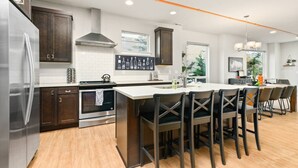 A modern kitchen with dark wooden cabinets, a stainless steel refrigerator, a built-in oven, and a large island with bar stools. - Wondrous Woodstock Townhouse, Huge Open Floor Plan, Custom Décor and Artwork, Four Miles to Portland (Portland)