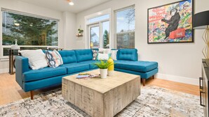 A modern living room with a blue sectional sofa, a wooden coffee table, and a colorful abstract painting on the wall. - Wondrous Woodstock Townhouse, Huge Open Floor Plan, Custom Décor and Artwork, Four Miles to Portland (Portland)