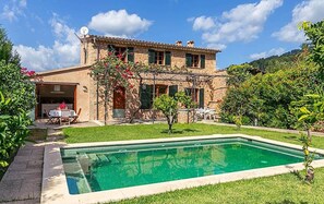 Un edificio de piedra de dos pisos con piscina, mobiliario exterior y jardín.