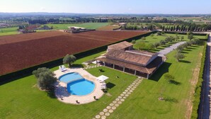 Vue aérienne d’une propriété comprenant une piscine, un grand bâtiment et des champs environnants.