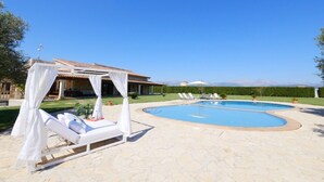 Un espace piscine avec des chaises longues, un coin salon abrité et un bâtiment en arrière-plan.
