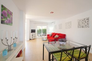 A modern living room with a glass dining table, a red sofa, and a TV in the background.
