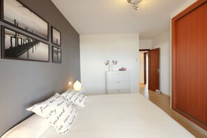 A bedroom with a bed, bedside table, dresser, and a door leading to another room.