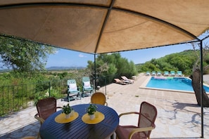A covered outdoor seating area with a pool and lounge chairs.