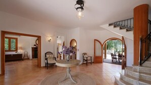 A spacious living area with a round table, chairs, a staircase, and a view of the outdoors. - Chalet "Sa Corbaia Nova" with Mountain View, Pool, Wi-Fi, Terraces & Garden (Artà)