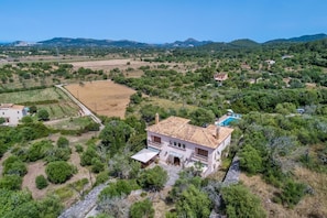 Una villa con techo de tejas, rodeada de vegetación y colinas.