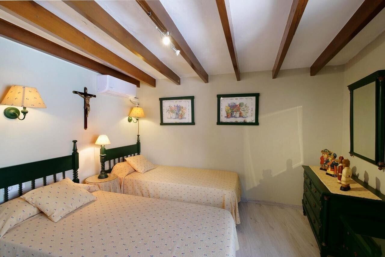 Een kamer met twee bedden, een houten plafond, wandlampen, ingelijste afbeeldingen en een dressoir met beeldjes.
