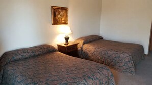 Une chambre avec deux lits, une table de chevet avec une lampe et un tableau encadré au mur.