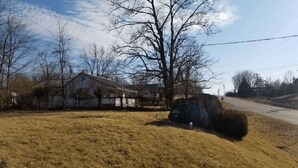 A rural landscape with a house, a large rock, and a grassy field. - Unity Lodge Suite 7 (Golconda)