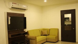 Una sala de estar con un televisor de pantalla plana, un sofá amarillo, un mueble de entretenimiento de madera oscura y una puerta con espejo.