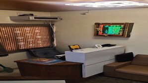 Una habitación con escritorio, sofá, un cuadro en la pared y ventana con persianas.