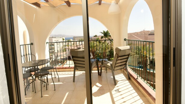 A balcony with a table and chairs, a view of the city, and a pergola providing shade. - shohamseaview (Eilat)
