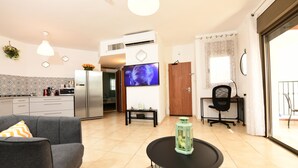 A modern living room with a sofa, a round table, and a TV. There is a kitchen area with a refrigerator and a dining table. - shohamseaview (Eilat)