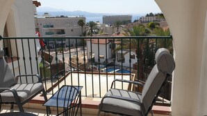 A balcony with two chairs and a small table, overlooking a swimming pool and buildings. - shohamseaview (Eilat)