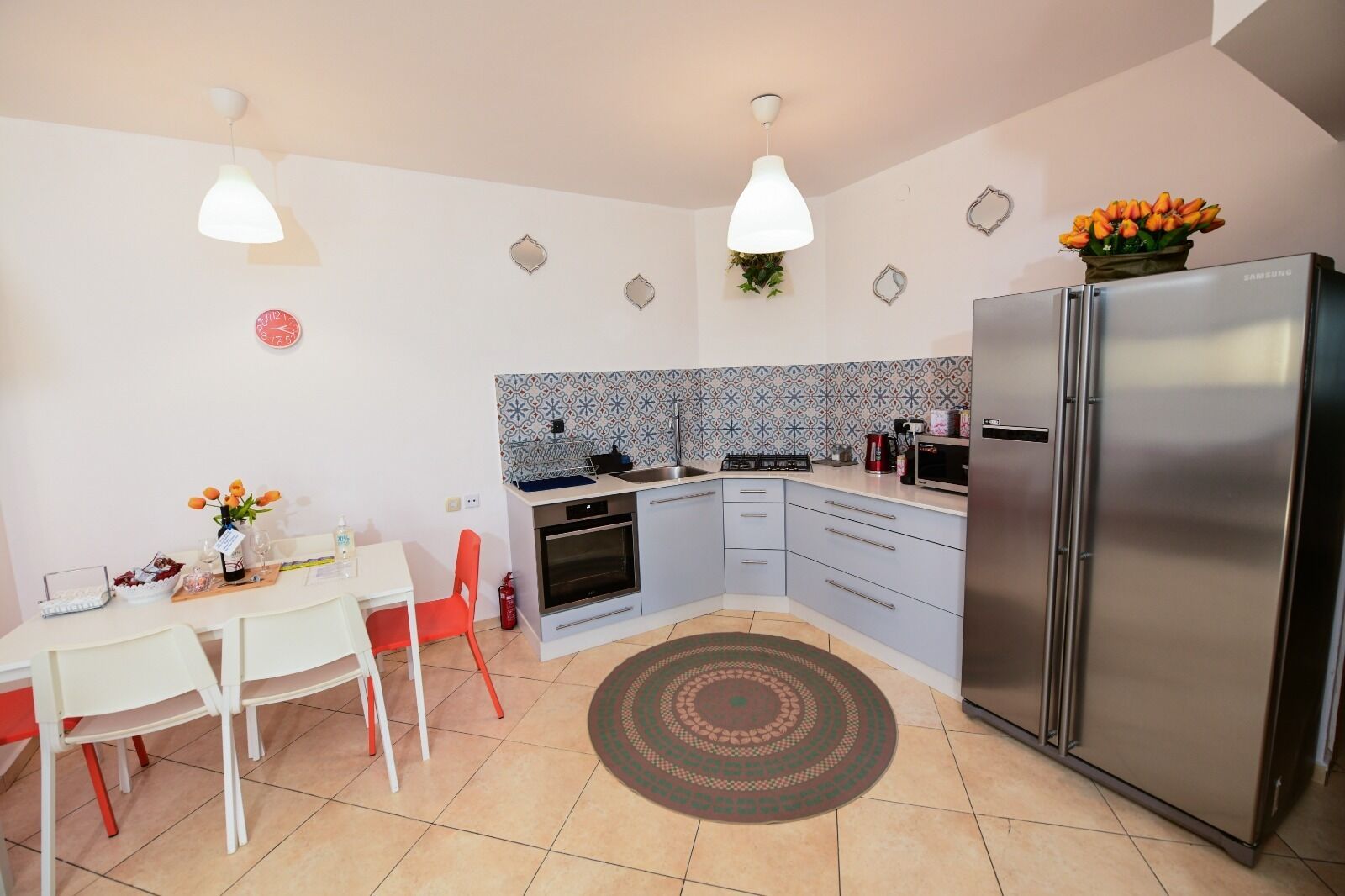 A compact kitchen with a refrigerator, stove, and sink. There is a dining table with chairs and a small rug.