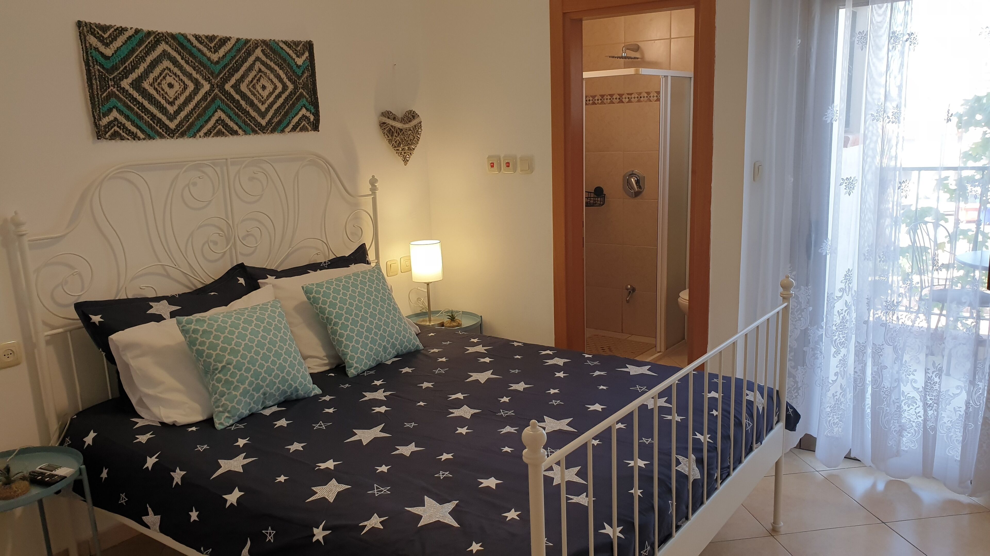 A bedroom with a bed, a nightstand, a wall-mounted heart decoration, and a bathroom door.