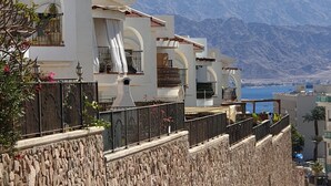 A modern building with balconies, a stone wall, and a view of mountains. - shohamseaview (Eilat)