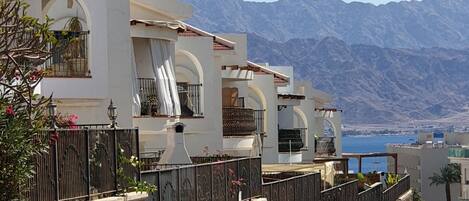 A modern building with balconies, a stone wall, and a view of mountains.