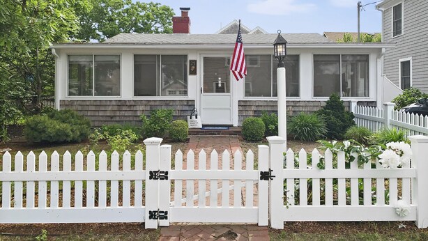 Una casa con cerca blanca, una bandera estadounidense y un buzón.