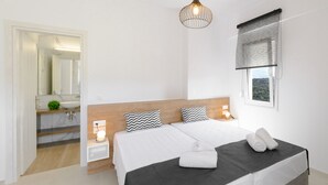 A modern bedroom with a large bed, bedside lamps, a hanging light fixture, a window with a view, and a bathroom with a sink and mirror. - Luxury Villa Oasis, 11 bedrooms, Private Heated Pool & Jacuzzi (Rethymno)