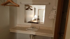 A bathroom with a sink, mirror, towel rack, and a hanging clothes rack.