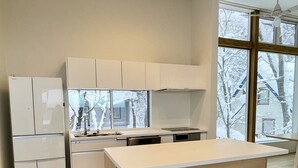 A modern kitchen with a central island, bar stools, and a view of a snowy landscape through large windows. - Sanzan Chalet (Hakuba)