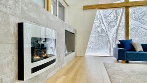 A modern living room with a stone fireplace, a large TV, and a blue sofa. - Sanzan Chalet (Hakuba)
