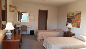 Une chambre avec deux lits, un bureau avec une chaise, un miroir et un tableau au mur.