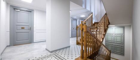 A hallway with a patterned floor, a wooden staircase, and a door with a number plate.