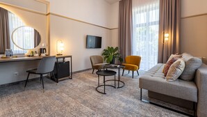 A modern hotel room with a sofa, a desk with a chair, a small table, a TV, and a large window with curtains. - MR67 Mayera Rapaporta  (Kraków)