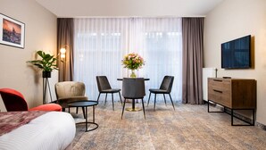 A hotel room with a bed, a desk with a chair, a small table with a vase of flowers, a TV, and a dresser. - MR67 Mayera Rapaporta  (Kraków)
