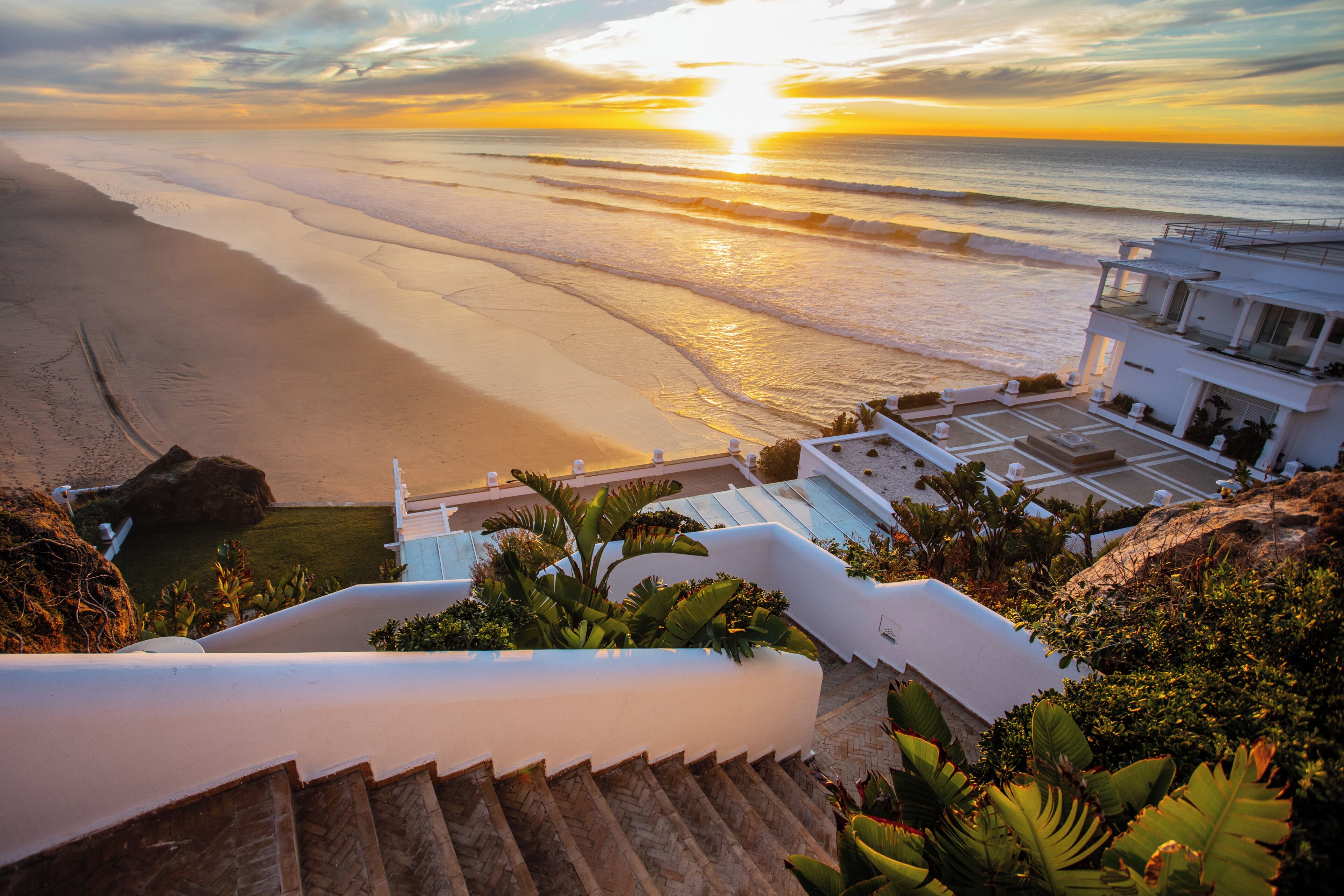 Un hotel frente al mar con una escalera que lleva a un balcón con vistas a la playa y al océano.