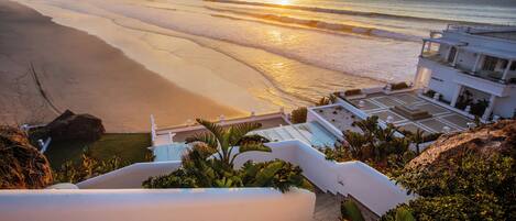 A coastal hotel with a staircase leading to a balcony overlooking the beach and ocean.