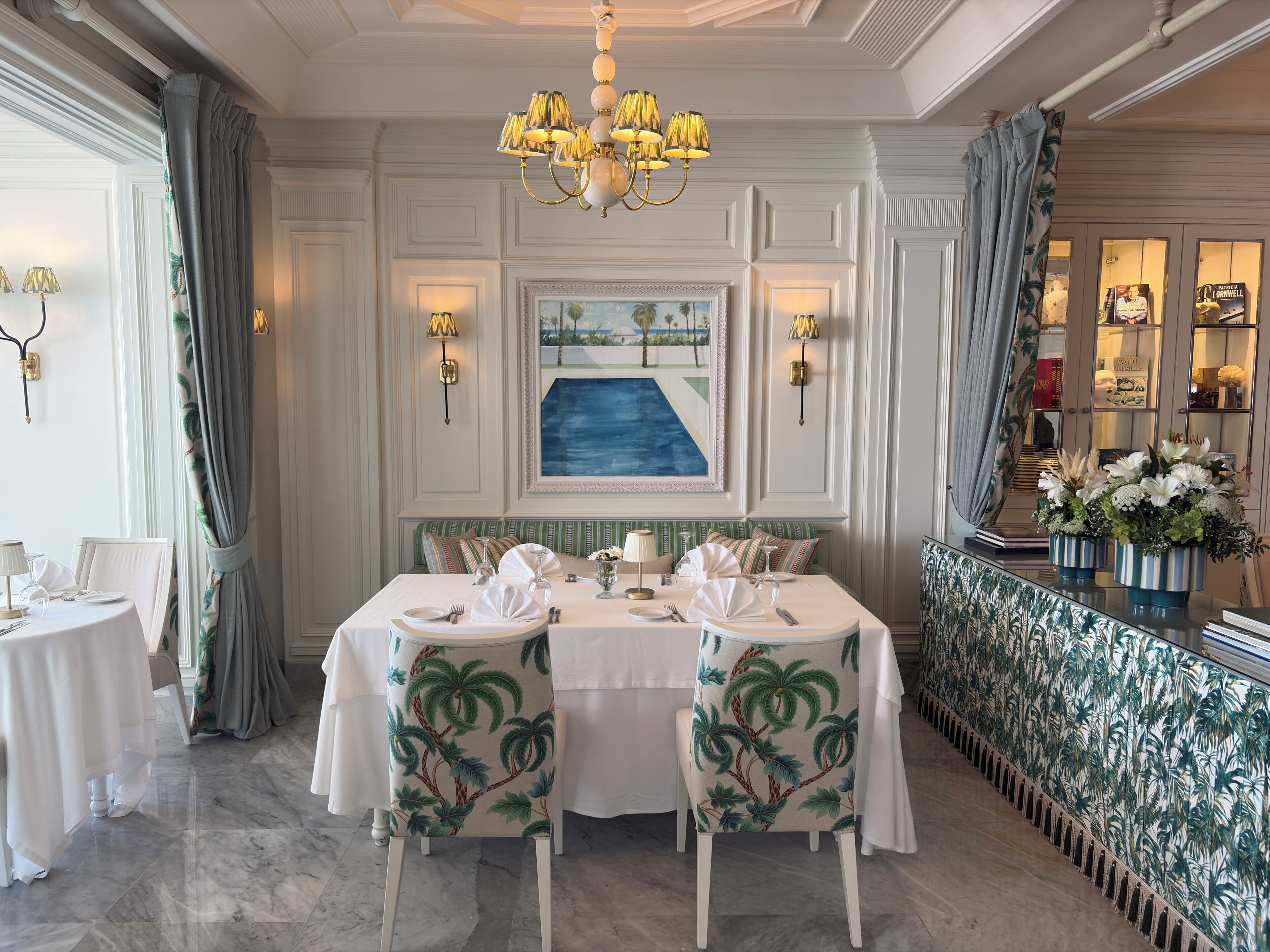 A formal dining room with a table set for four, a chandelier, and a painting above the table.