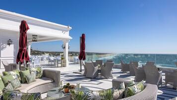 A rooftop terrace with outdoor seating, a white pergola, and a view of the ocean.